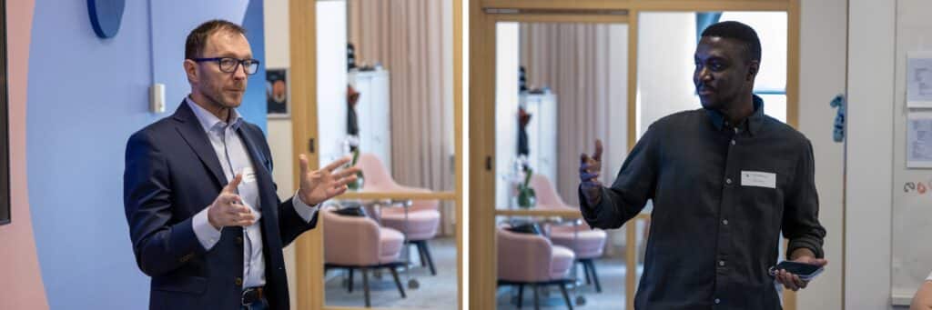 Två personer står i ett mötesrum och pratar inför deltagare.